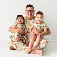 Father holding his two children wearing matching Caramel Ready to Rodeo pajamas. Dad is wearing men's Caramel Ready to Rodeo men's pajama top paired with matching men's pajama pants. His kids are wearing Caramel Ready to Rodeo in short sleeve and shorts and zippy styles