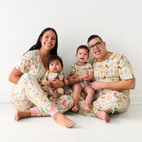 Family of four wearing coordinating Ready to Rodeo pajamas. Mom is wearing women's Pink Ready to Rodeo women's pj top and matching pj pants. Dad is wearing men's Caramel Ready to Rodeo men's pj to and matching pj pants. Their children are wearing Caramel Ready to Rodeo in two piece shorts and short sleeve and shorty zippy styles