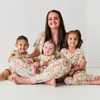 Mother sitting holding her children. Mom is wearing women's Pink Ready to Rodeo women's pj top and matching pj pants. Her daughter is wearing a matching two piece pajama set. Her boys are wearing a crescent and shorty zippy Caramel Ready to Rodeo