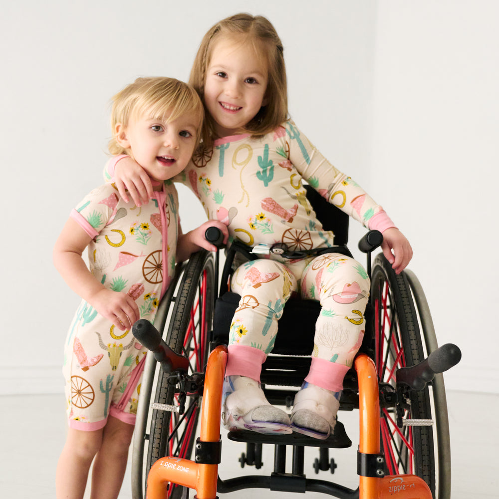 Two children posing together wearing matching Pink Ready to Rodeo in shorty zippy and two piece pajama styles