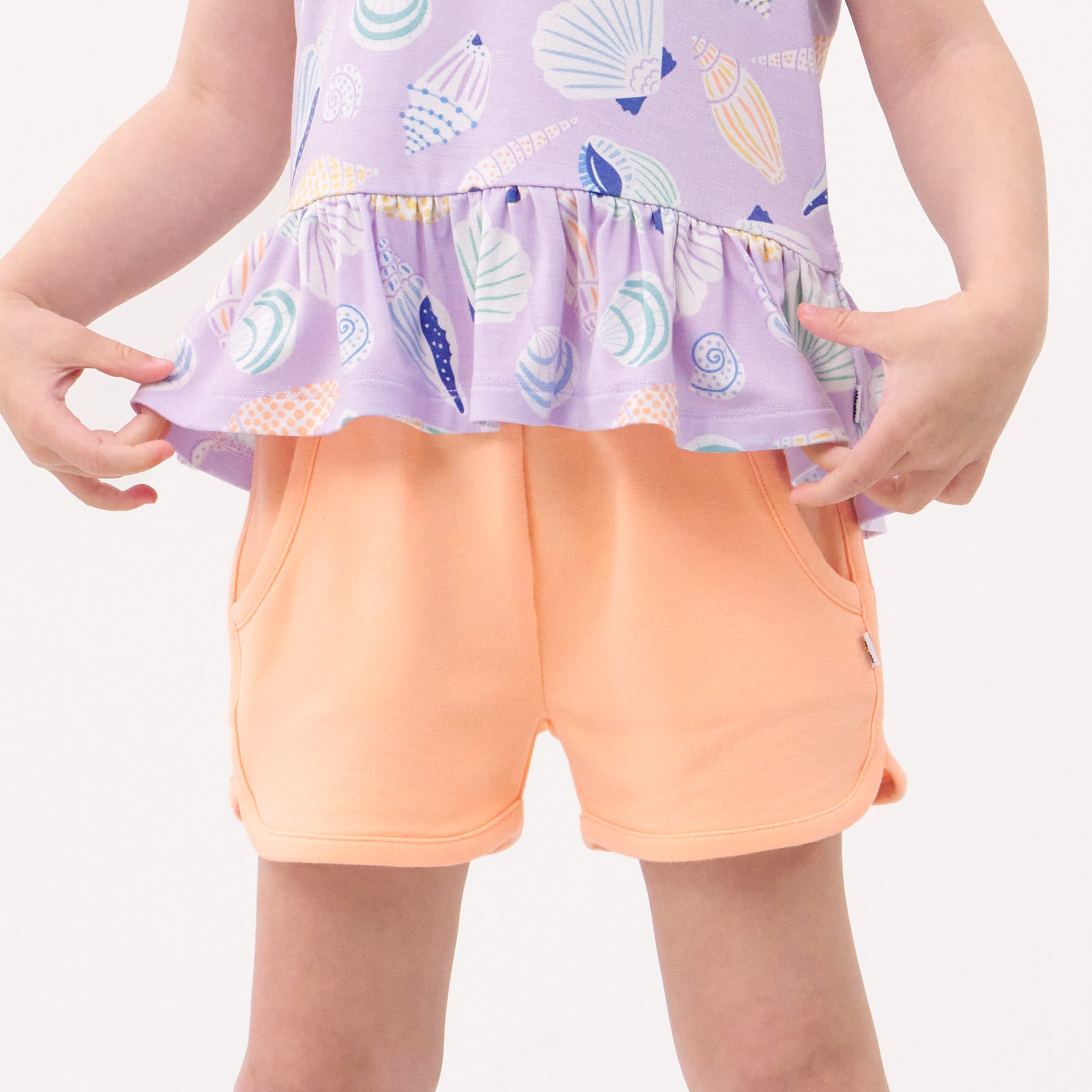 Close up image of a child wearing Peach Nectar dolphin shorts and coordinating Play top