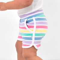 Close up side view image of a child wearing Rainbow Stripes dolphin shorts