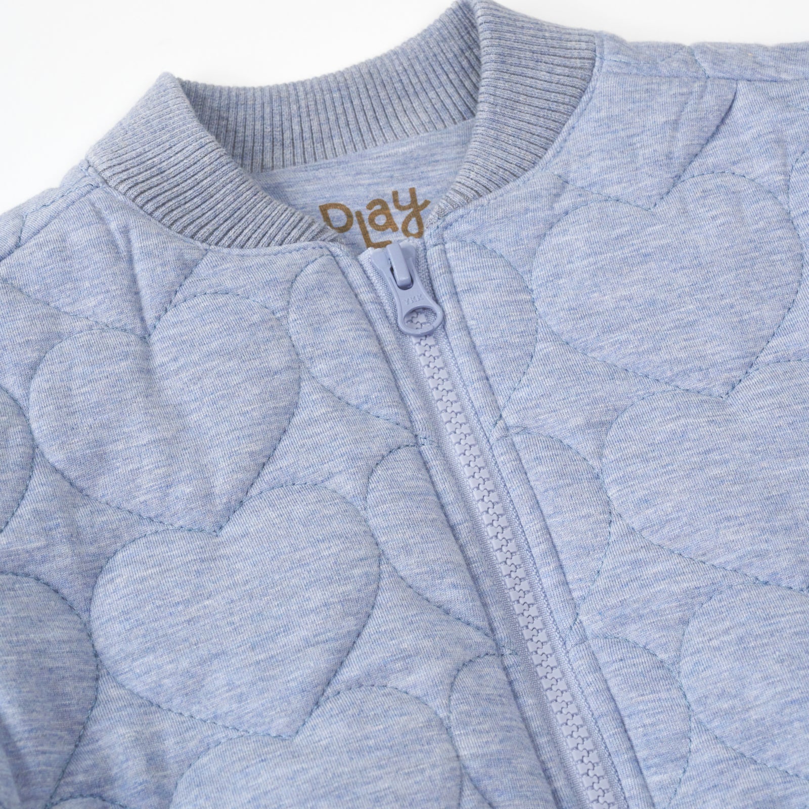 close up flat lay of a light blue denim quilted varsity jacket