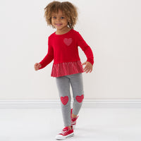Child wearing a Candy Red peplum tee and coordinating heart patch leggings