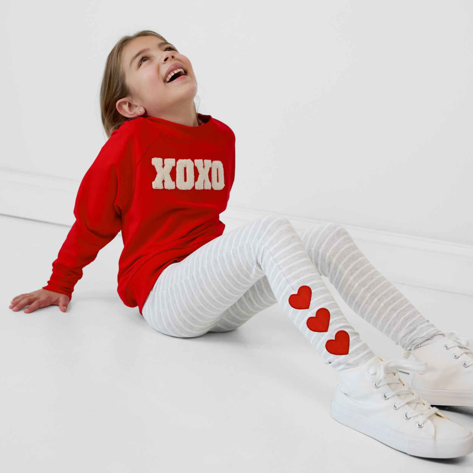 Child sitting on the ground wearing Heart Patch Leggings and a coordinating Crewneck Sweatshirt