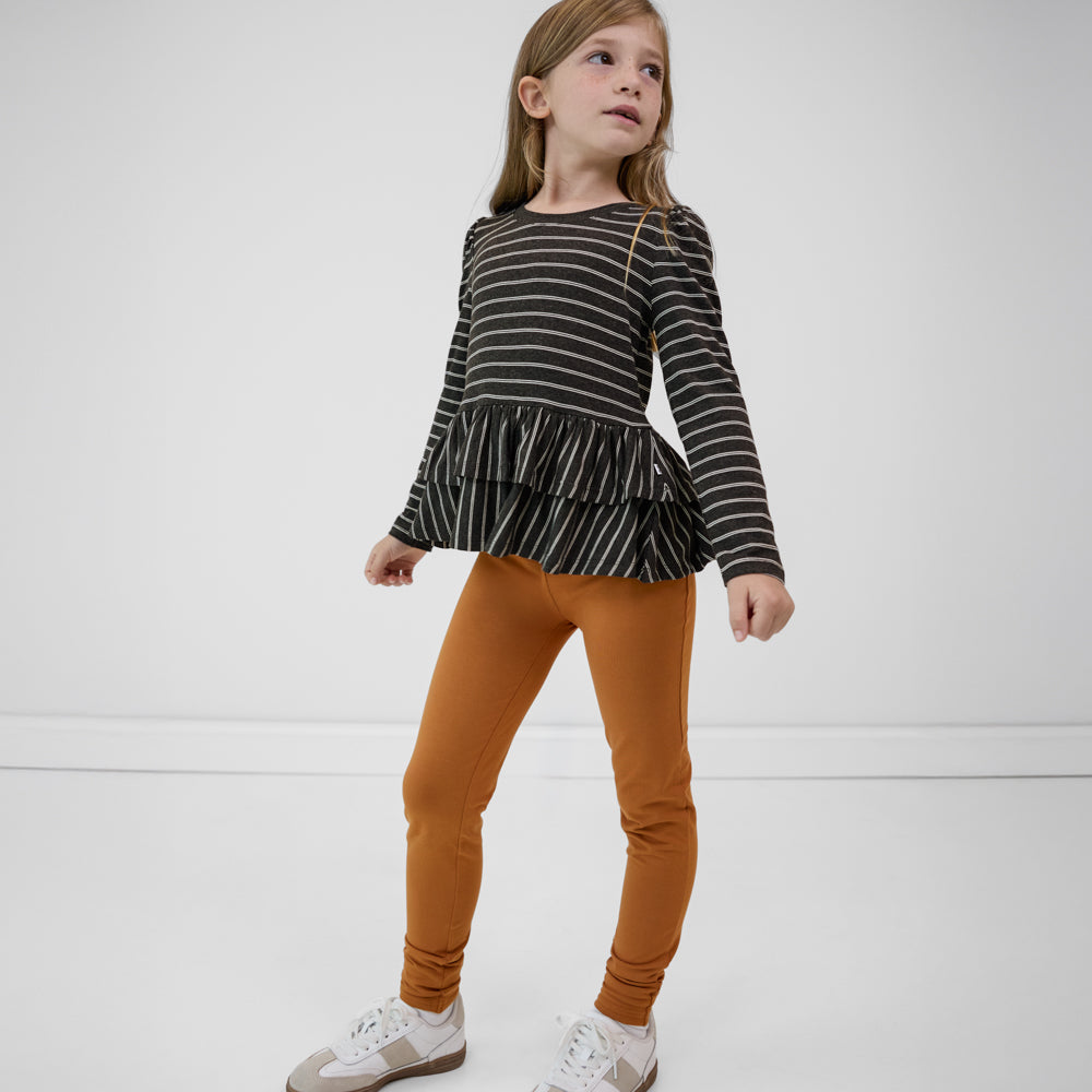 Child wearing Golden Brown girls leggings paired with a black striped long sleeve peplum top