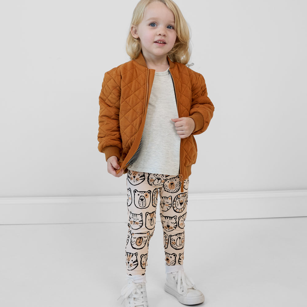 Child wearing Lions, Tigers & Bears leggings paired with a gray top and golden brown quilted varsity jacket