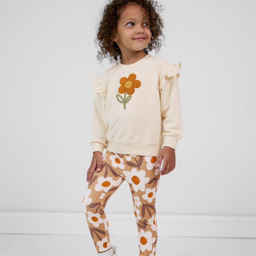 Child looking to the side wearing Daisy Daydream leggings paired with an off-white crewneck