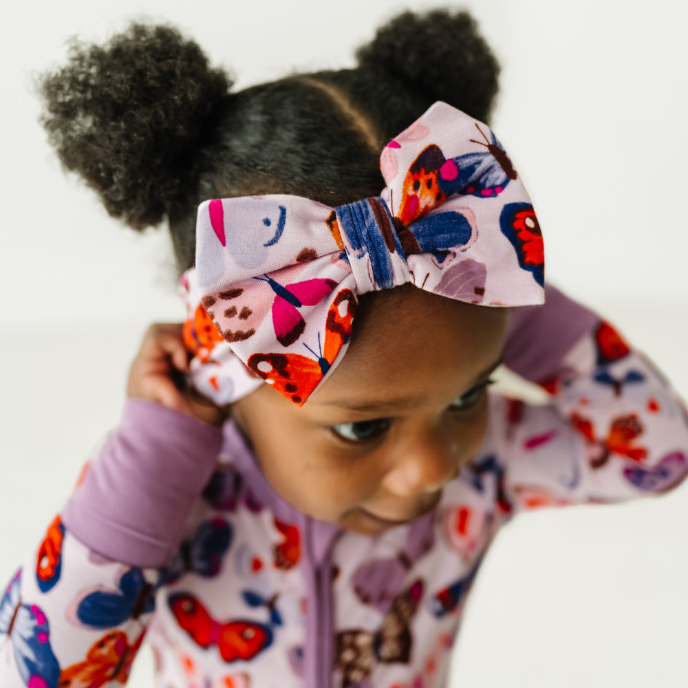 Close up image of a child wearing a Butterfly Kisses luxe bow headband and matching zippy
