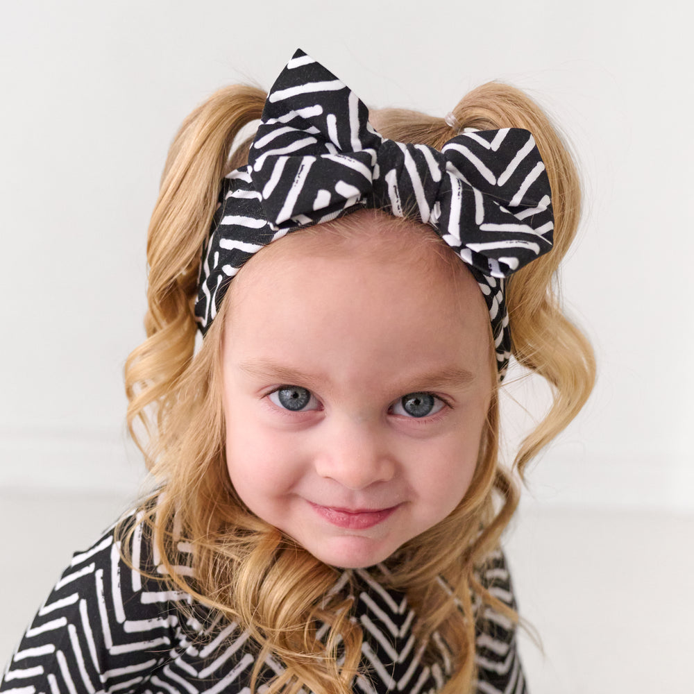Close up image of a child wearing a Monochrome Chevron luxe bow headband and matching pajamas