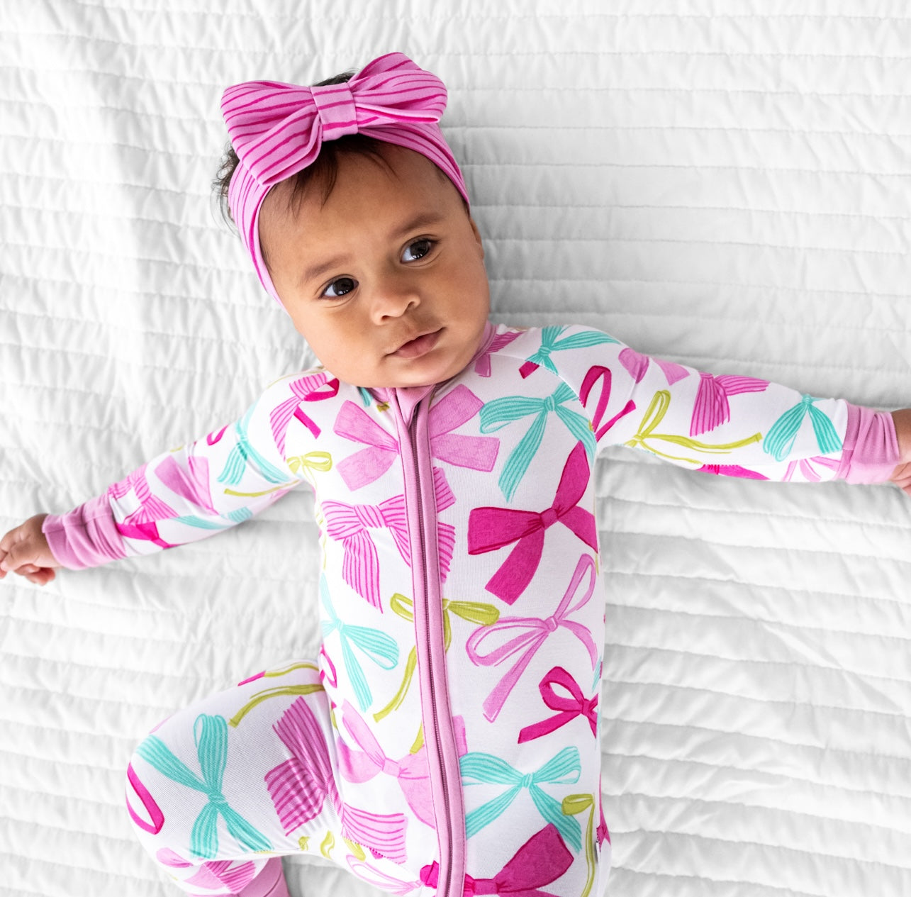 child laying on a bed wearing a Ribbons and Bows zippy paired with a Tonal Pink Stripes luxe bow headband