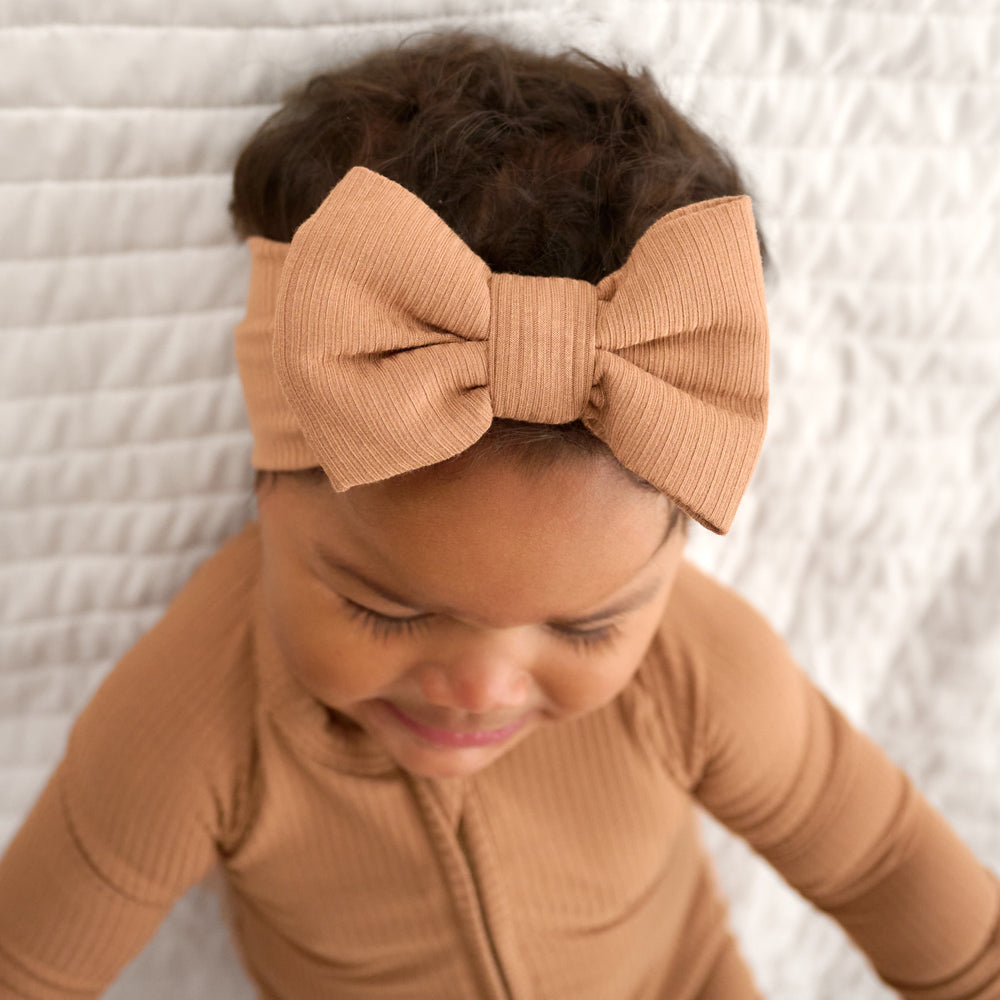 Close up image of baby wearing the Caramel Ribbed Luxe Bow Headband and Caramel Ribbed Zippy