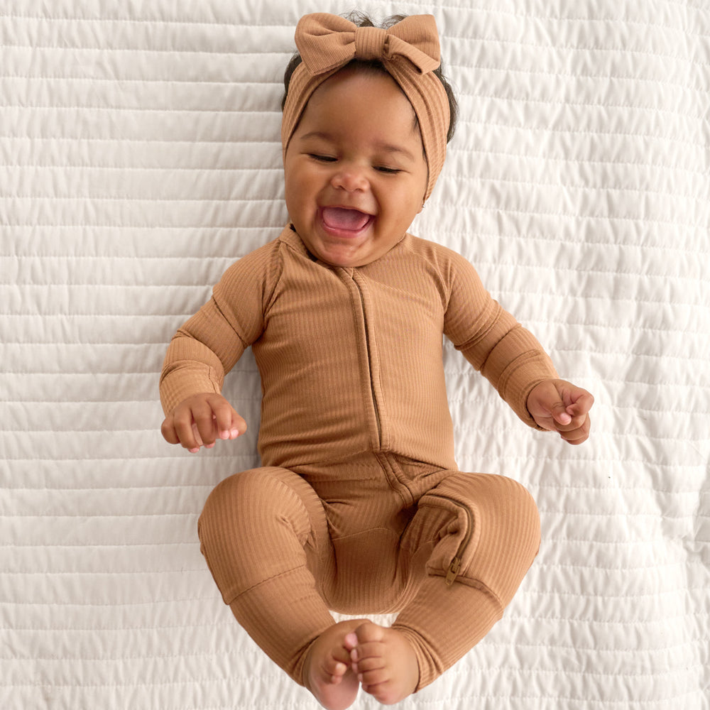 Top view image of baby laying down and laughing while wearing the Caramel Ribbed Luxe Bow Headband and Caramel Ribbed Zippy