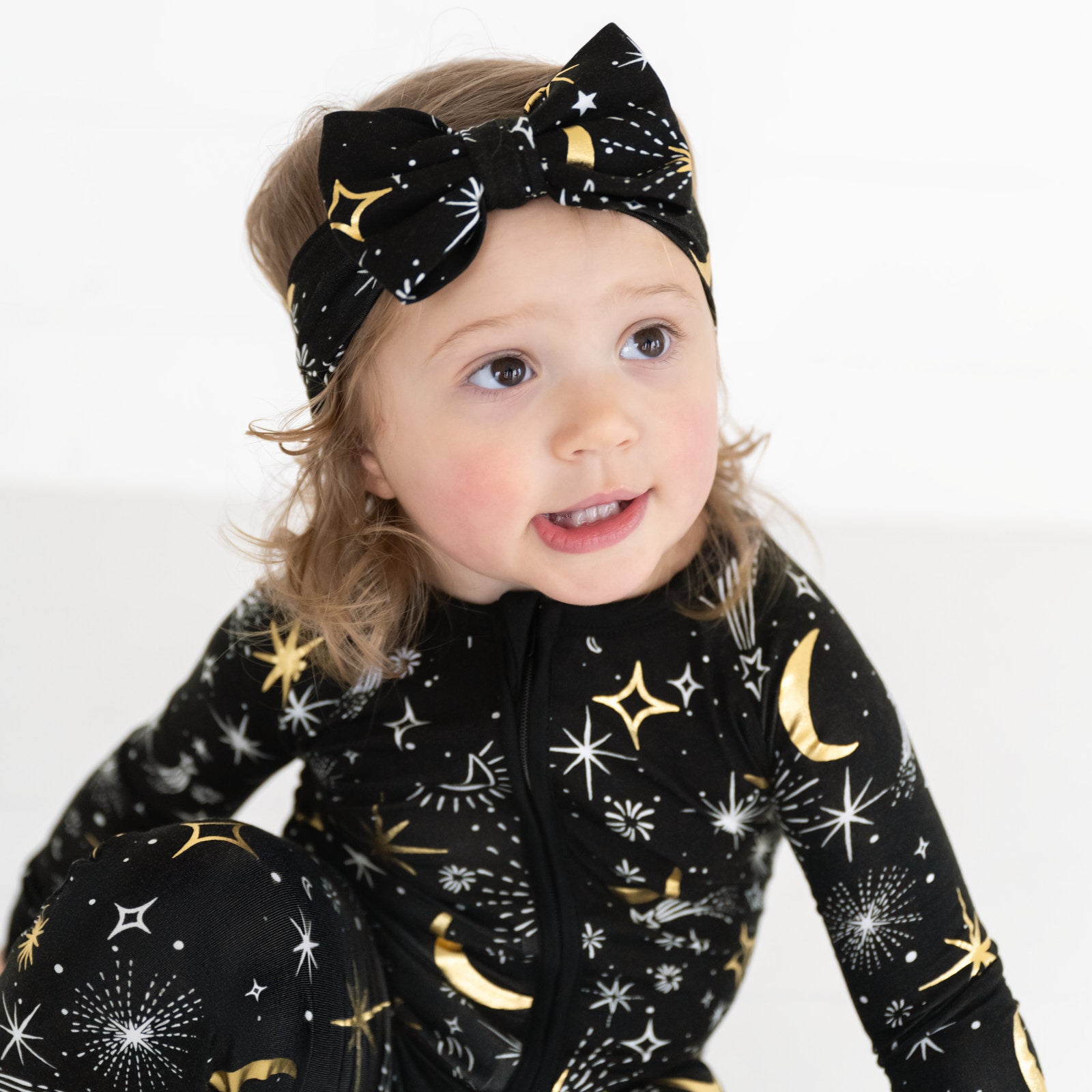 Close up image of a child wearing a Celebration Stars luxe bow headband and matching zippy