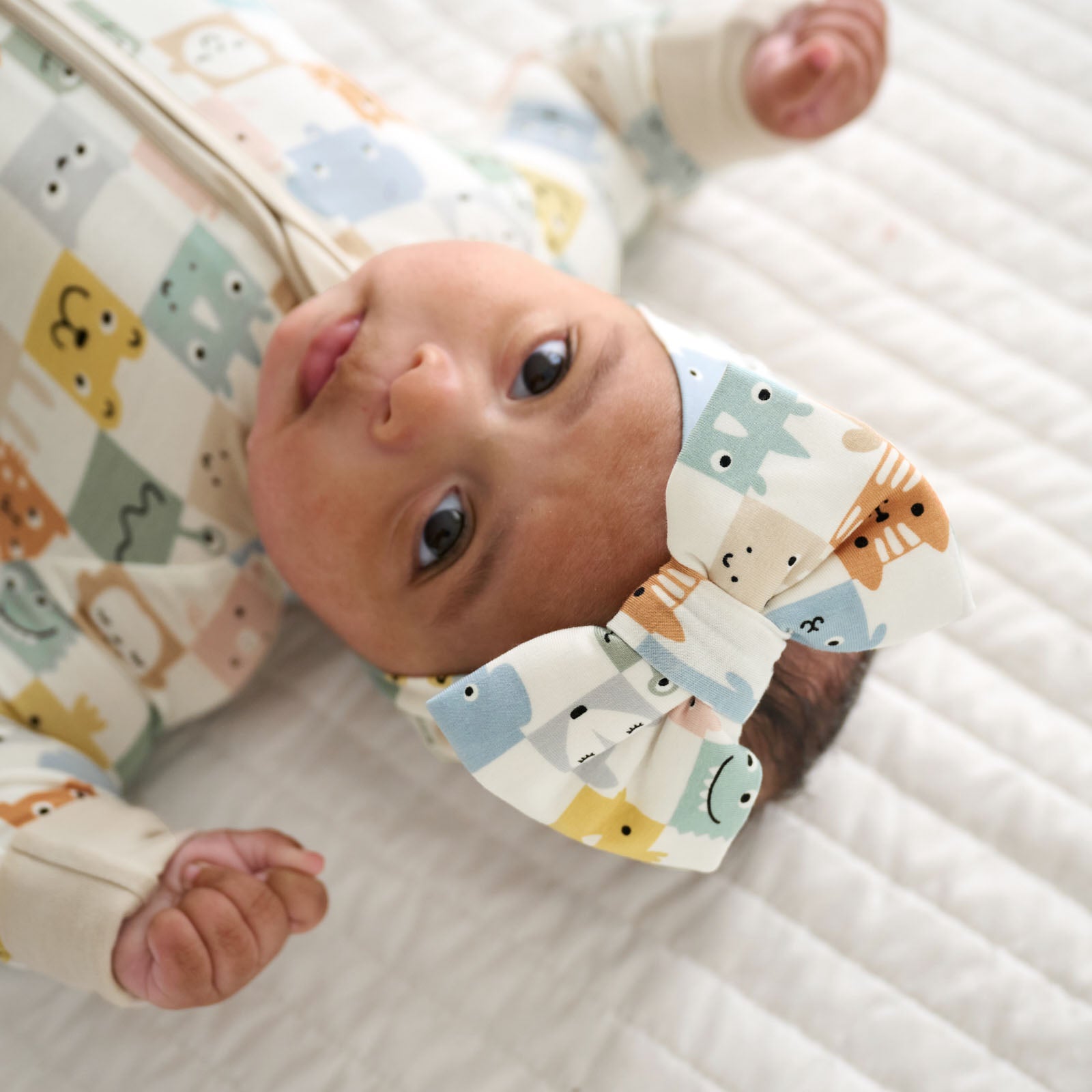 Close up image of a child laying on a blanket wearing a Check Mates luxe bow headband and matching zippy