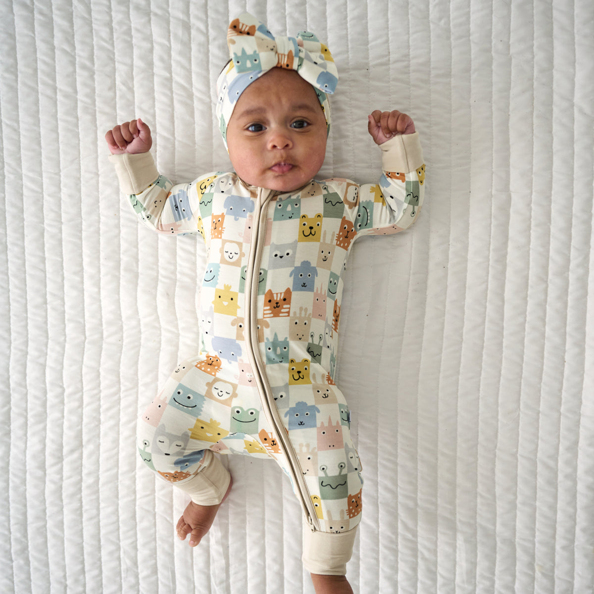 Child laying on a blanket wearing a Check Mates luxe bow headband and matching zippy