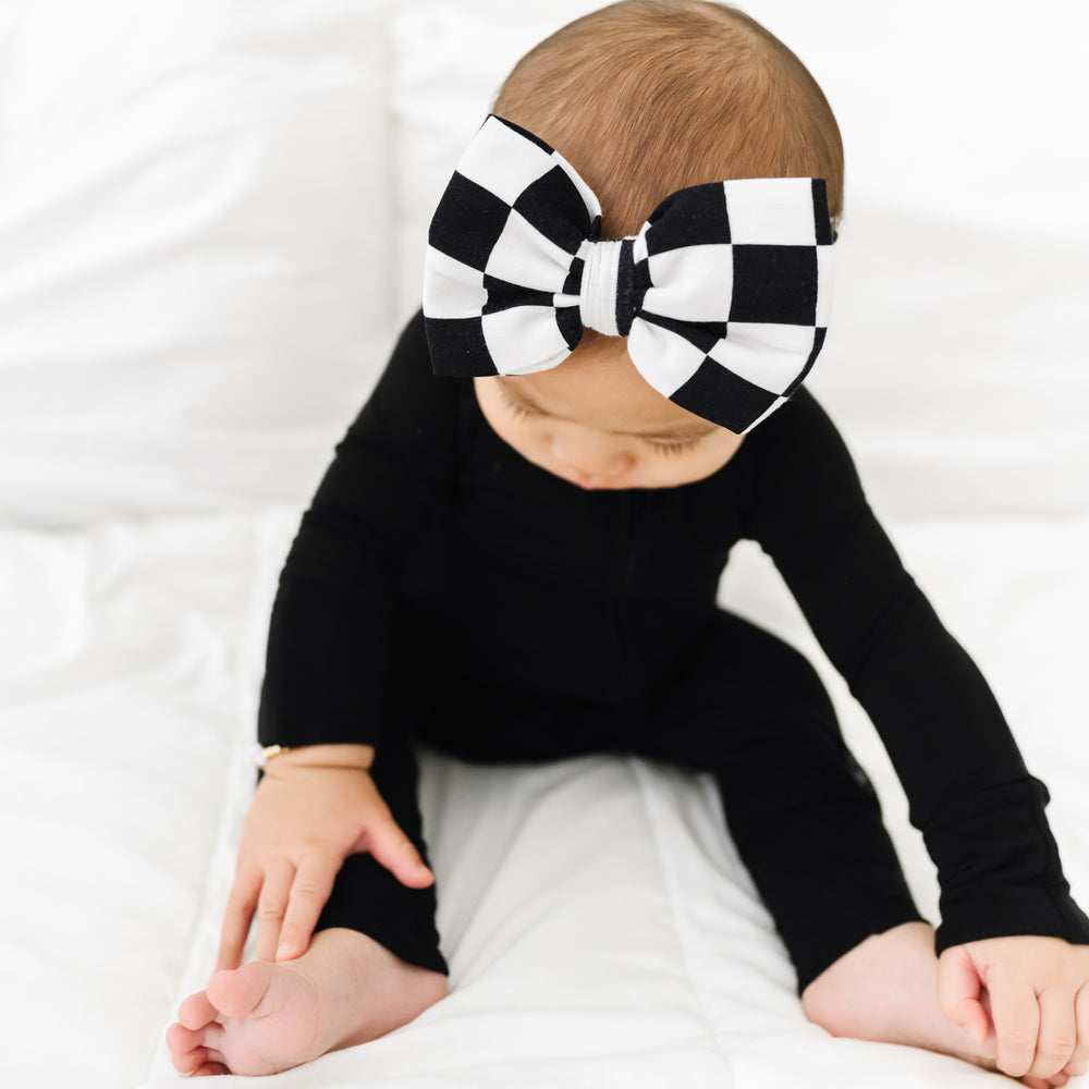 Close up image of a child wearing a Cool Checks luxe bow headband and black zippy