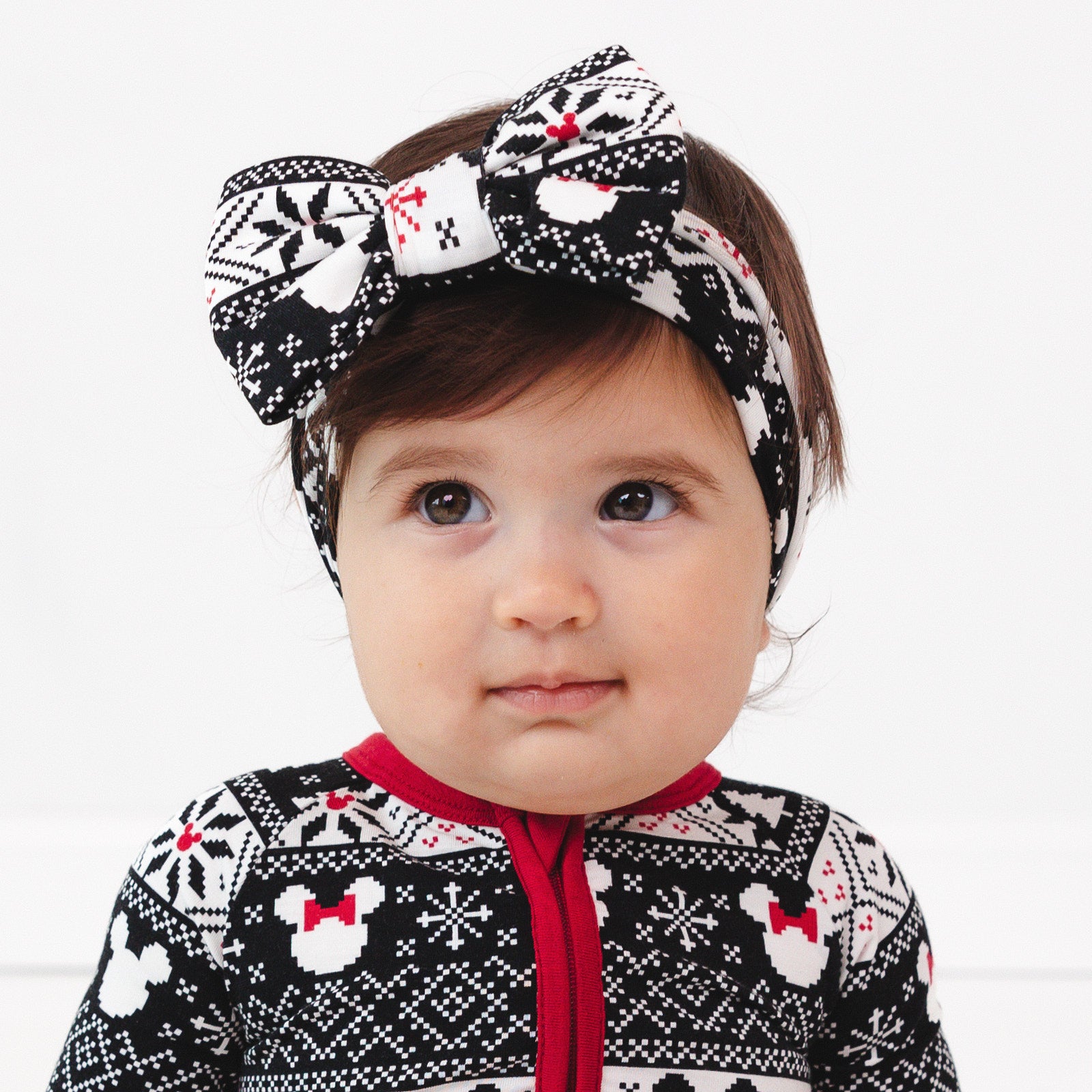 Child laying on a bed wearing a Mickey Fair Isle luxe bow headband. Child is wearing a matching Mickey Fair Isle zippy