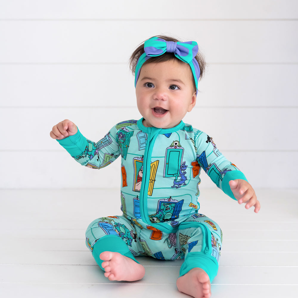 Smiling baby sitting while wearing the Disney Monsters, Inc. Sulley Luxe Bow Headband and Disney Monsters, Inc. Zippy