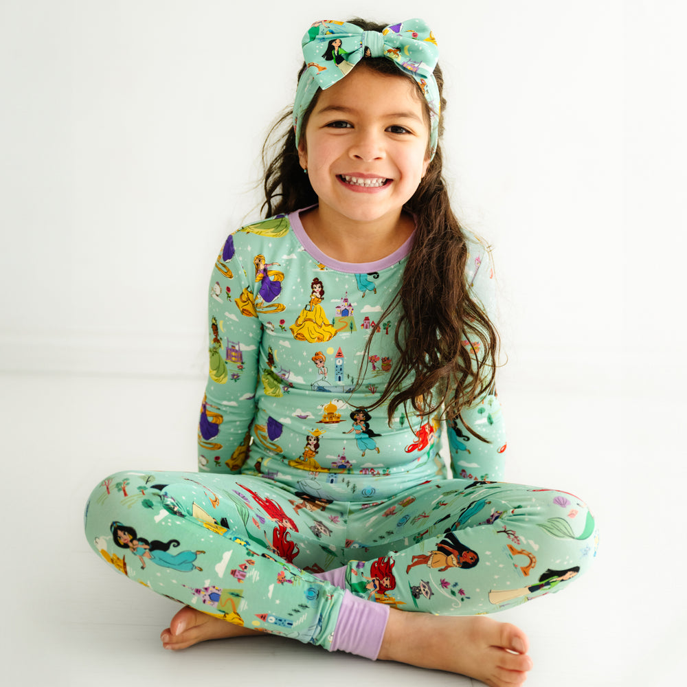 Child sitting on the ground wearing a Disney Princess Dreams luxe bow headband and matching pajamas
