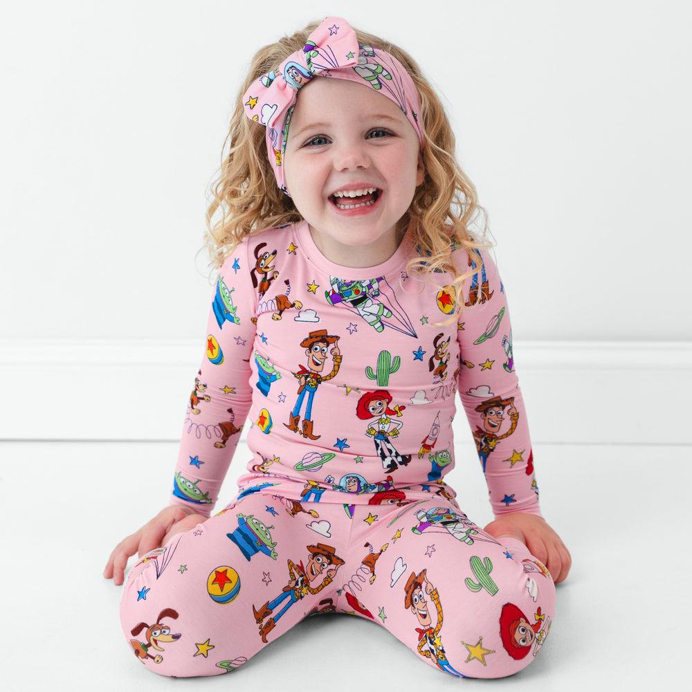 Image of a child wearing Pink Toy Story Stars two piece pj set wearing a matching luxe bow headband