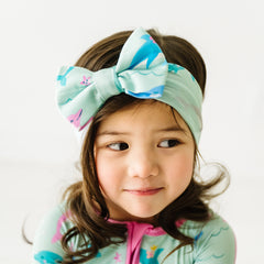 Close up image of a child wearing a Dolphin Dance luxe bow headband and matching zippy