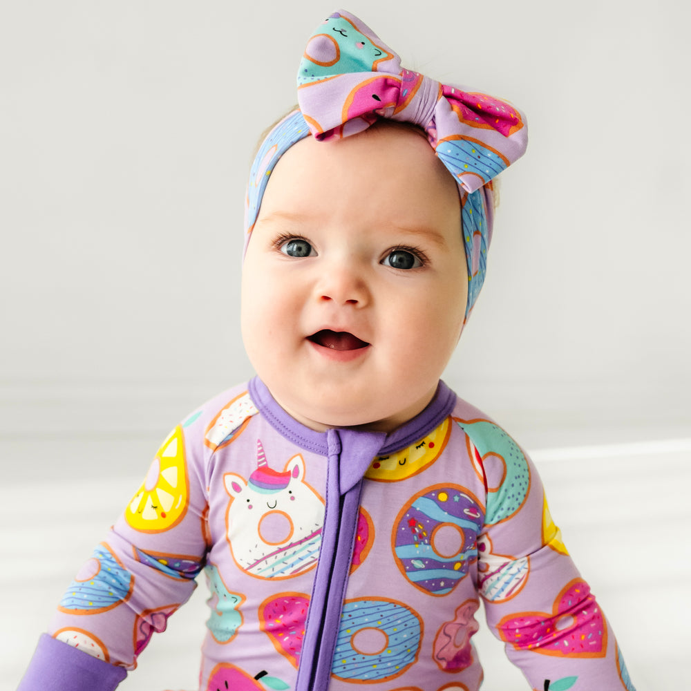 Click to see full screen - Child wearing a Lavender Donut Dreams luxe bow headband and a matching zippy