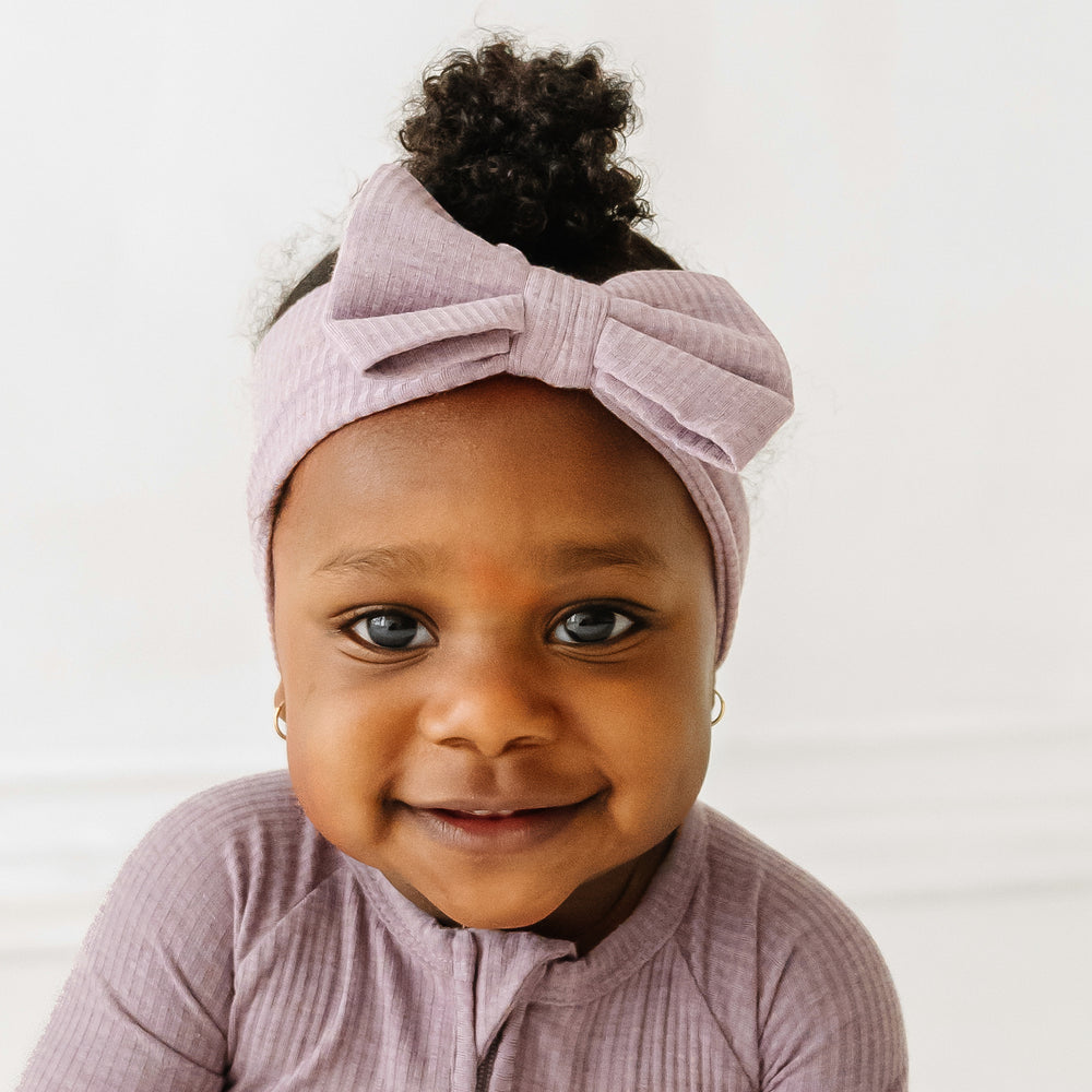Close up image of child wearing a Heather Smokey Lavender Ribbed luxe bow headband paired with a matching zippy