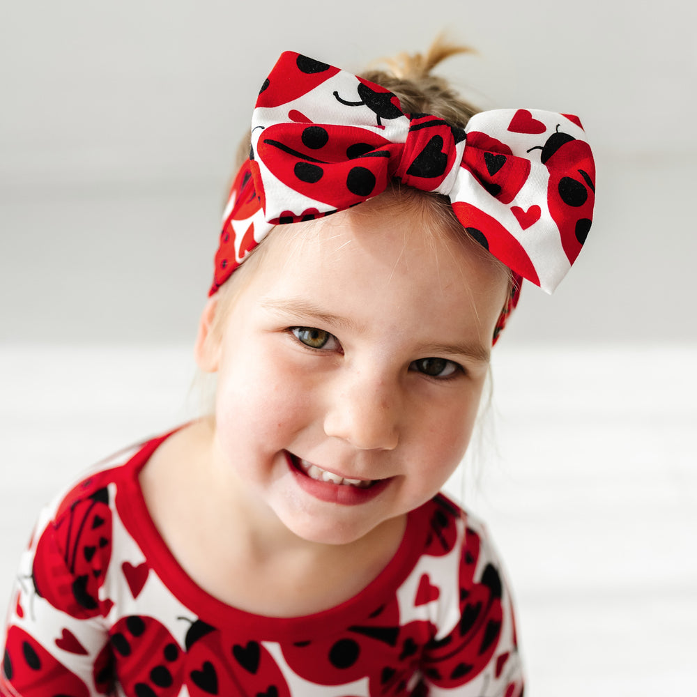Click to see full screen - Alternate close up image of a child wearing a Love Bug printed luxe bow headband and matching pajamas