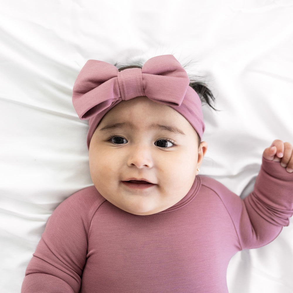 Child laying on a bed wearing a Dusty Plum luxe bow headband