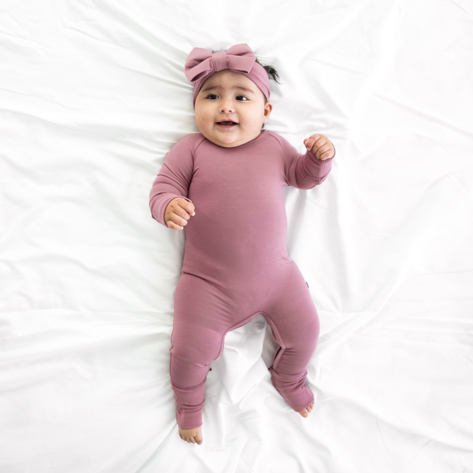 Child laying on a bed wearing a Cozy Dusty Plum Crescent Zippy paired with a matchign luxe bow headband