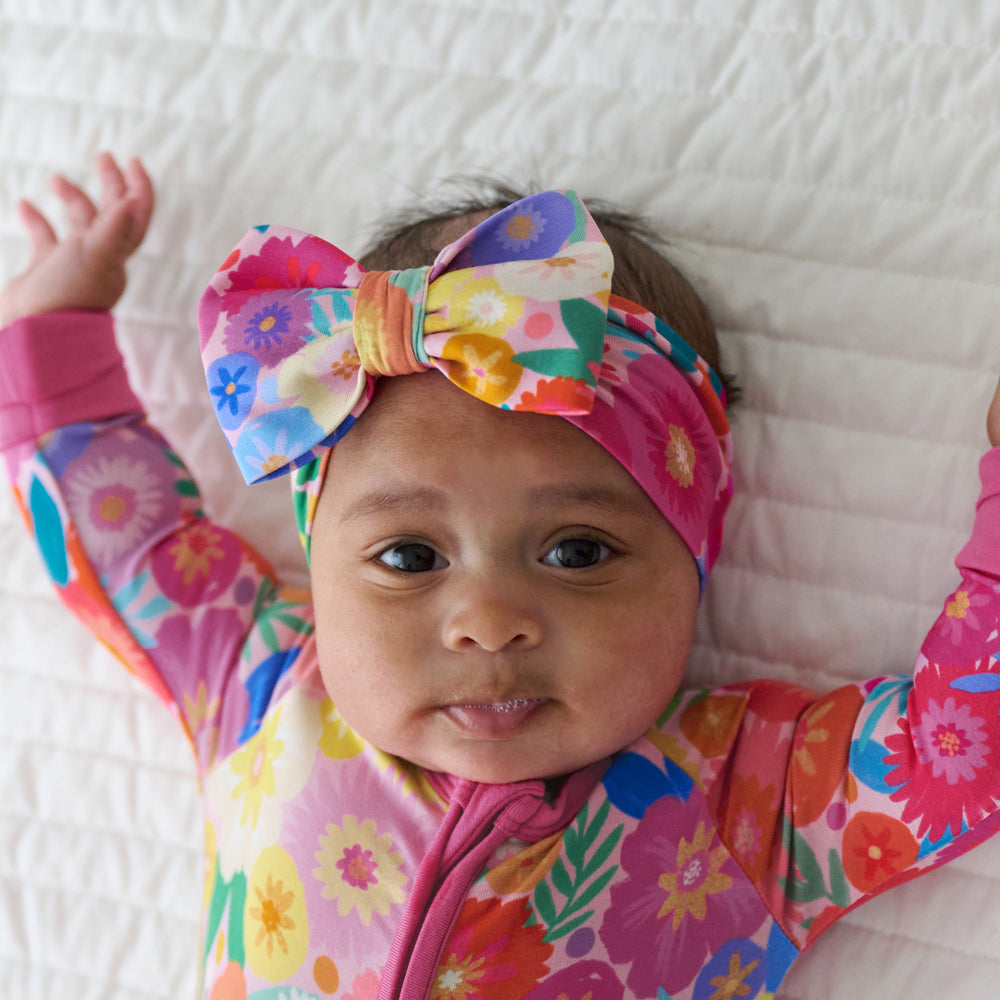 Close up image of a child wearing a Rainbow Blooms luxe bow headband and matching zippy