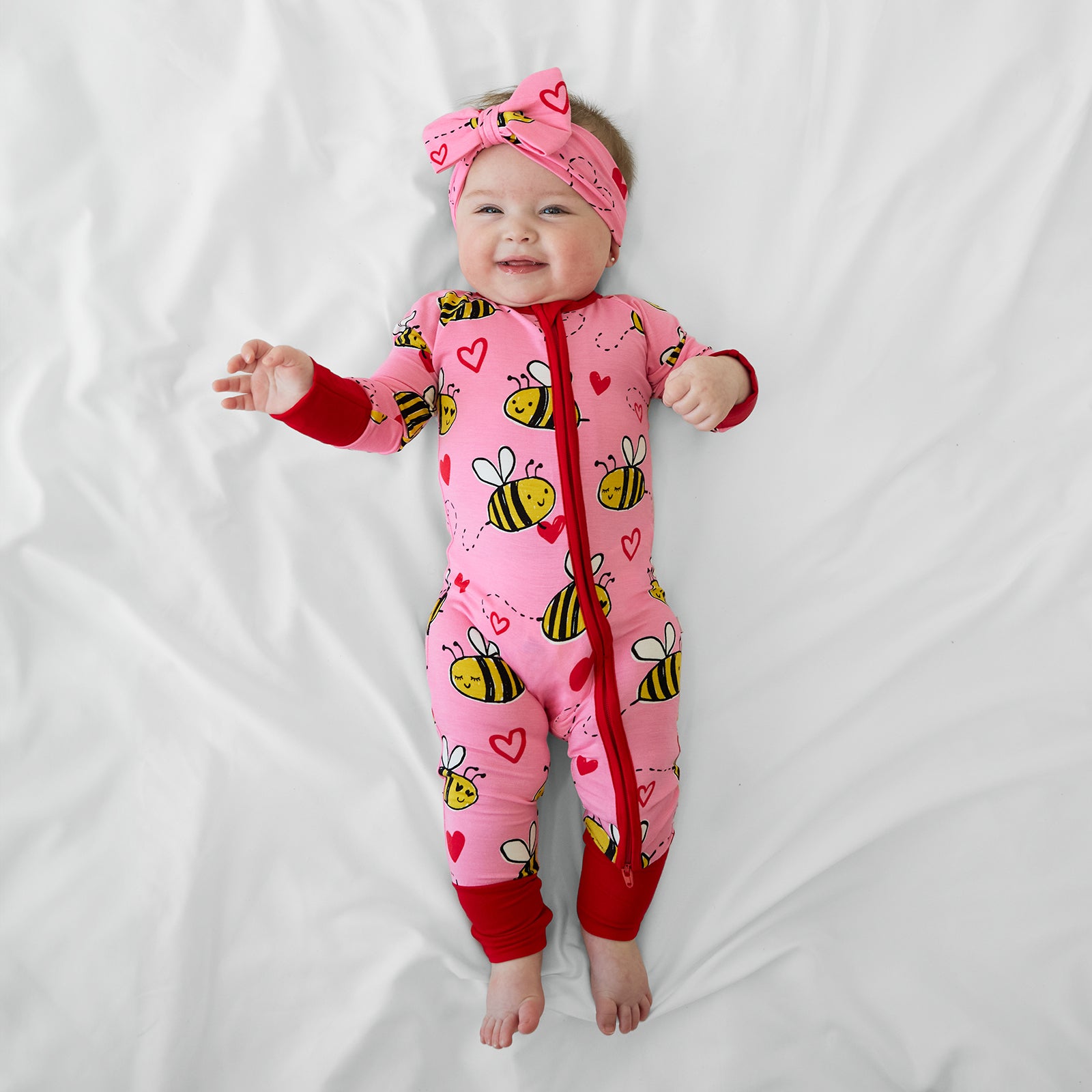 Image of a child laying on a bed wearing a Pink Bee Mine Zippy with a matching luxe bow headband