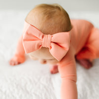 Close up image of a child wearing a Peach Luxe Bow headband