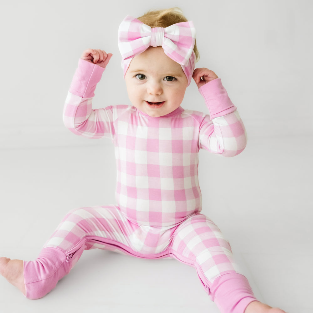 Click to see full screen - Child wearing a Pink Gingham crescent zippy paired with a matching luxe bow headband