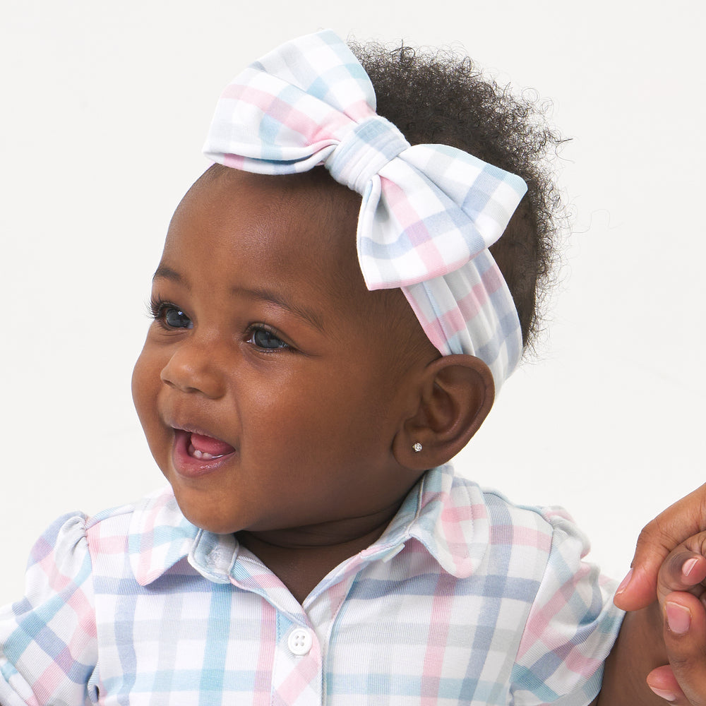 Close up image of a child wearing a Playful Plaid luxe bow headband and matching dress