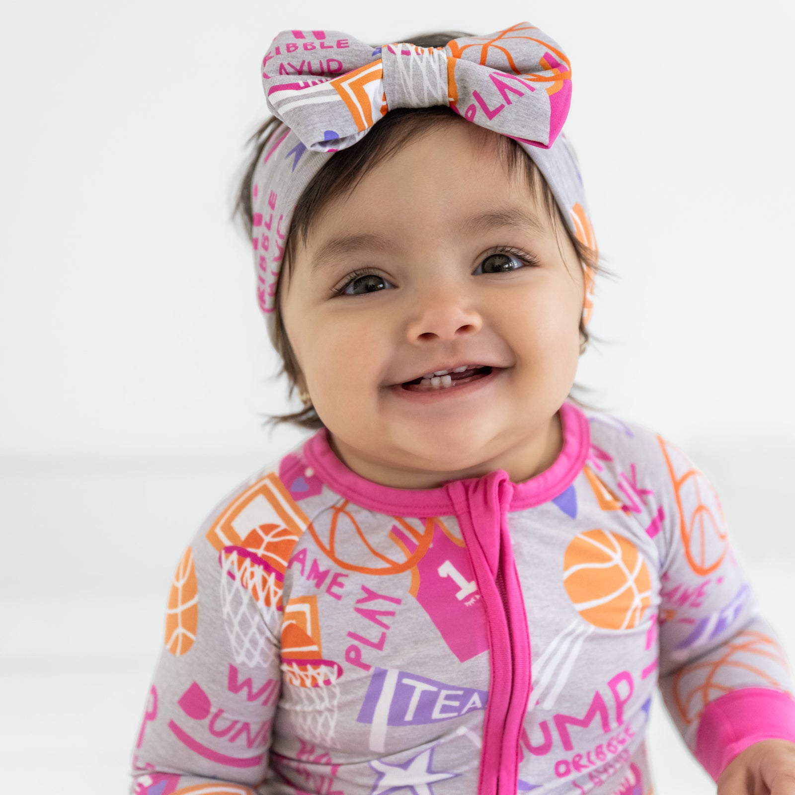 Child wearing the Pink Slam Dunk Luxe Bow Headband and matching bamboo baby pajamas