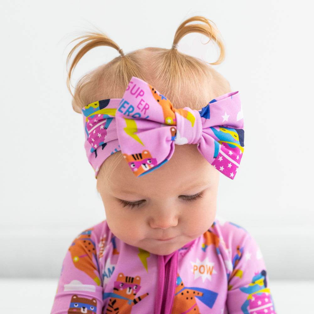 Child with head tilted down wearing a pink Sleepy Heroes zippy with a matching luxe bow headband