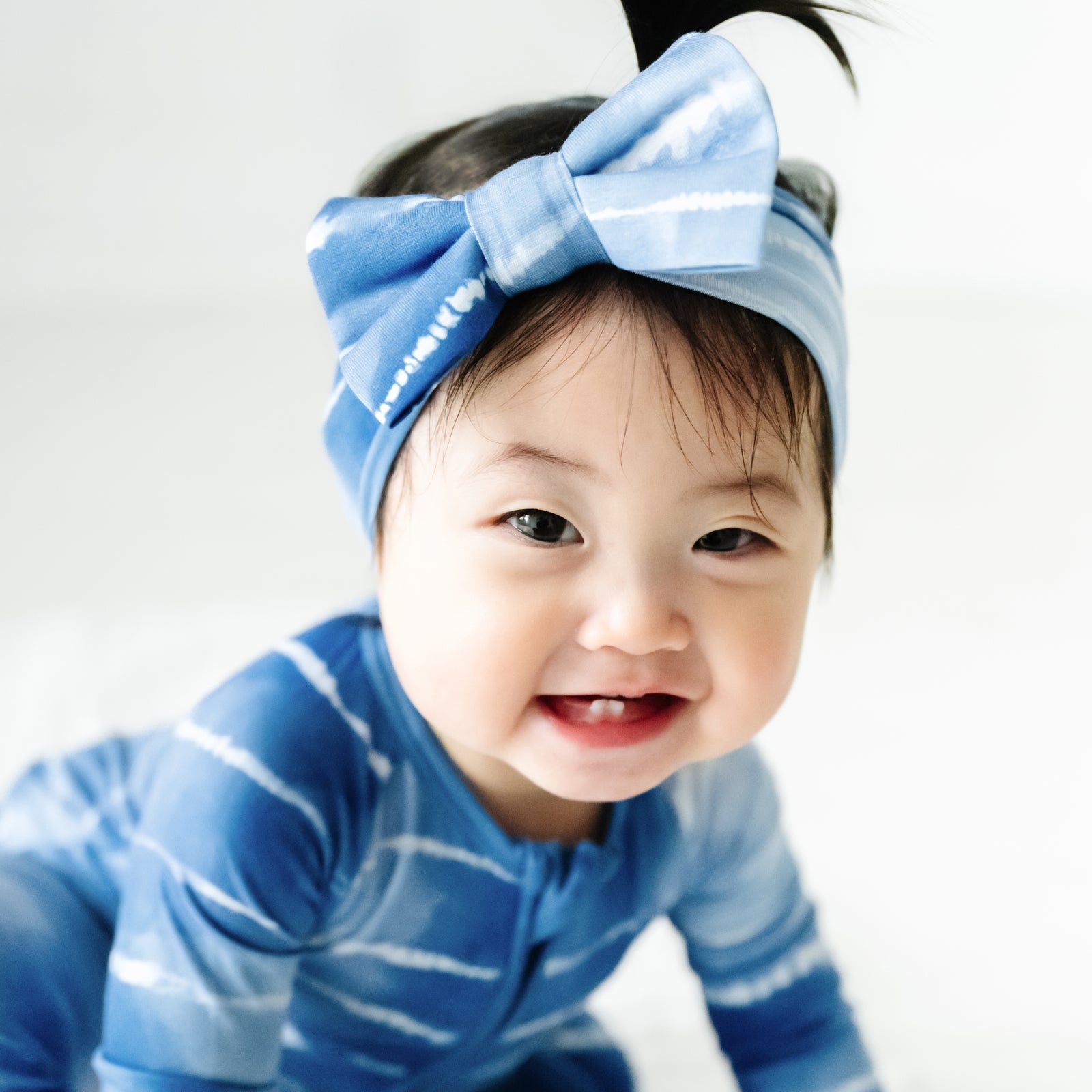Close up image of a child wearing a Blue Tie Dye Dreams luxe bow headband and matching zippy