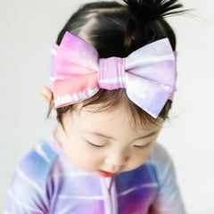 Close up image of a child wearing a Pastel Tie Dye Dreams luxe bow headband and matching zippy
