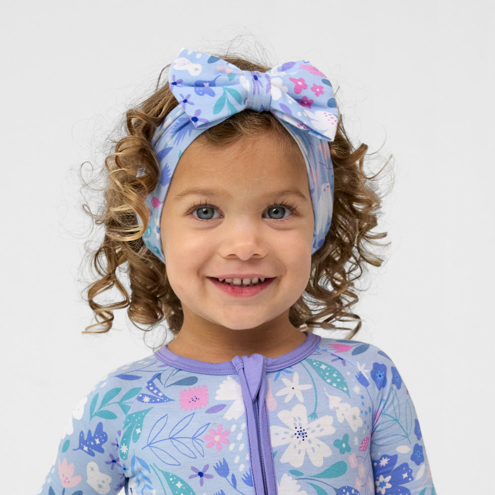 Close up image of a child wearing a Magical Meadow Luxe bow headband and a matching zippy