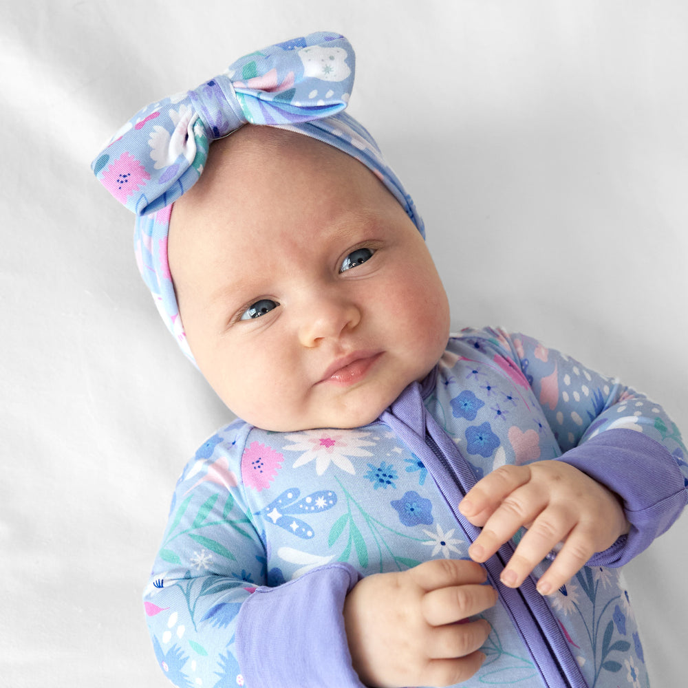 Image of a baby laying on a bed wearing a Magical Meadow luxe bow headband and matching zippy