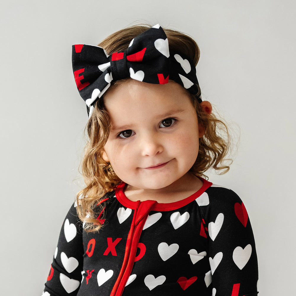 Click to see full screen - Close up image of a child wearing a Black XOXO luxe bow headband and matching zippy