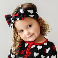 Alternate close up image of a child wearing a Black XOXO luxe bow headband and matching zippy