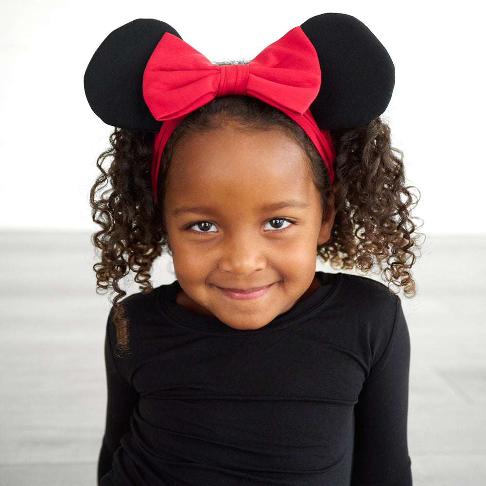 Close up image of a child wearing a Minnie Mouse Ear Luxe bow Headband in size 4-8