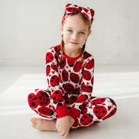 Child sitting on the ground wearing a Love Bug printed two-piece pajama set and matching luxe bow headband