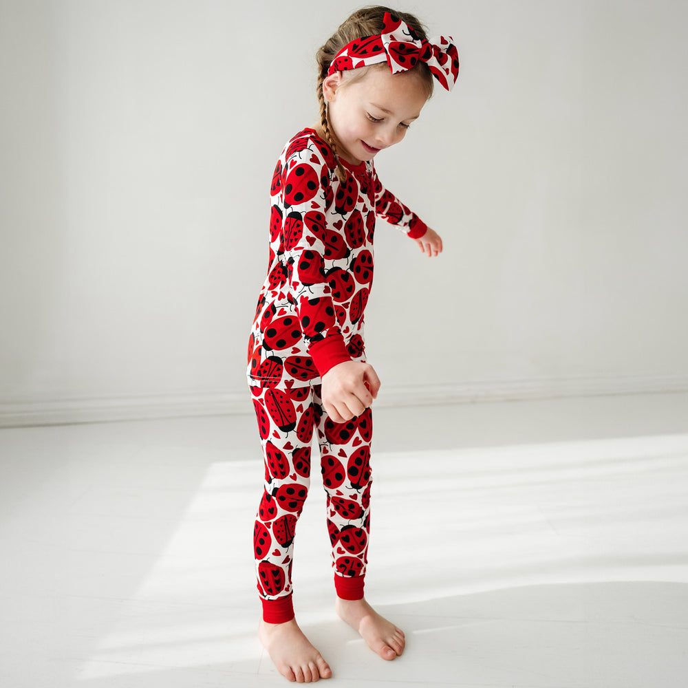 Click to see full screen - Child wearing a Love Bug printed luxe bow headband and matching pajamas