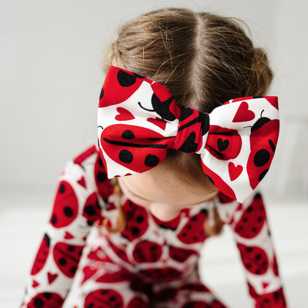 Click to see full screen - Close up image of a child wearing a Love Bug printed luxe bow headband and matching pajamas