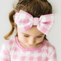 Close up image of a child wearing a Pink Gingham luxe bow headband
