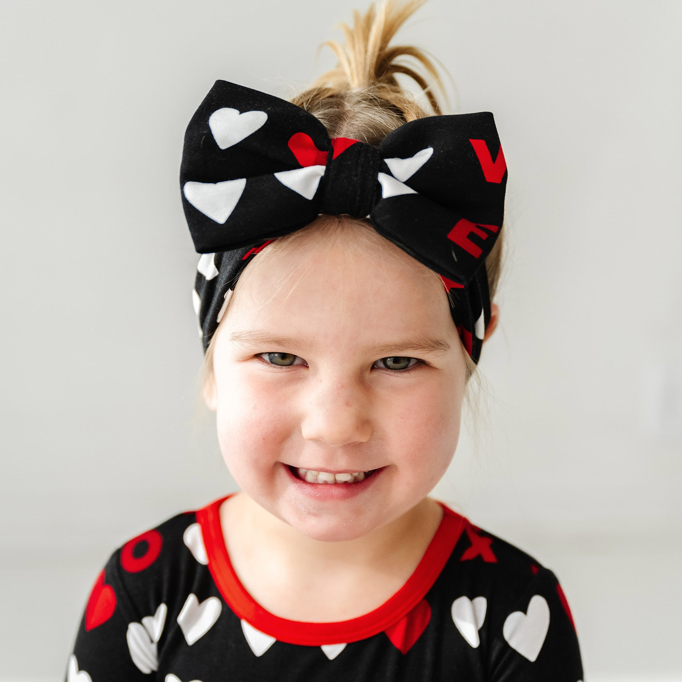 Third alternate close up image of a child wearing a Black XOXO luxe bow headband and matching zippy